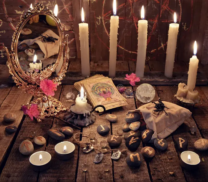 Mesa ritual con velas blancas, espejo, runas y cartas de tarot